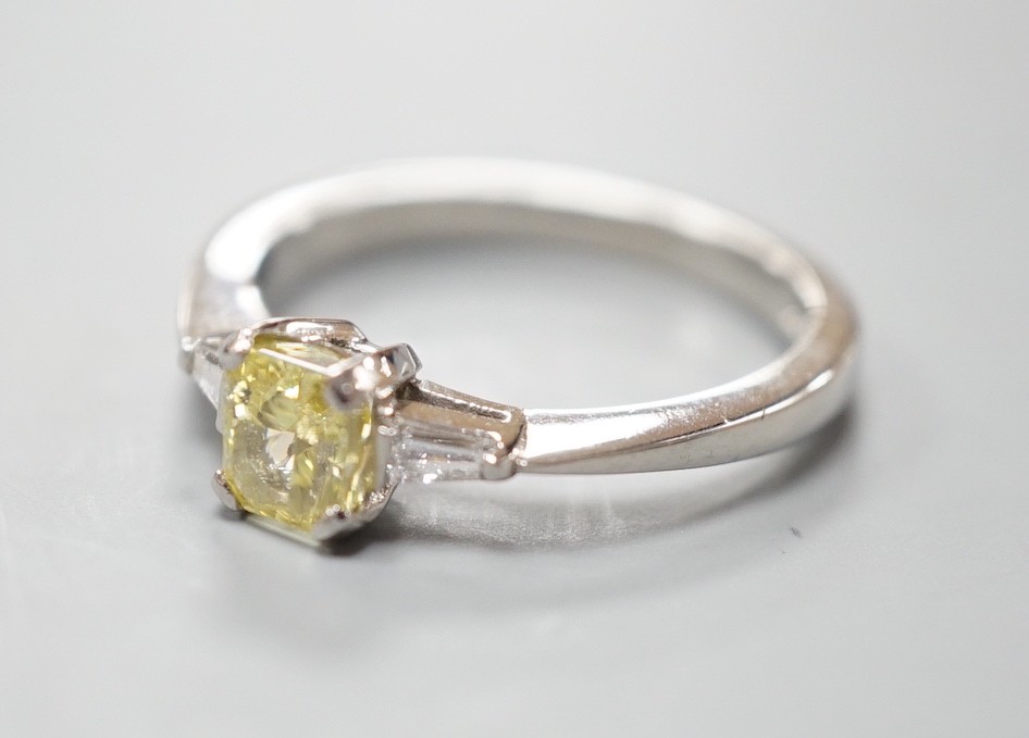 A modern platinum and single stone fancy yellow diamond set ring, with trapeze cut diamond set shoulders, size N, gross weight 4.6 grams